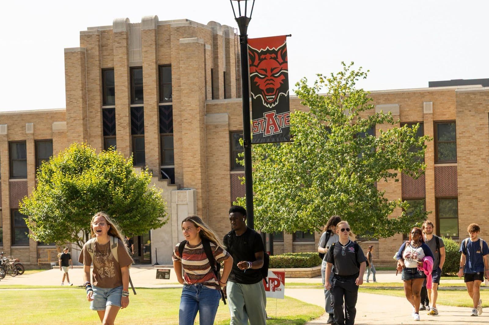 Sinh viên A-State đi bộ qua toà nhà Wilson Hall dưới lá cờ Red Wolves trong tuần đầu học kỳ mùa Thu