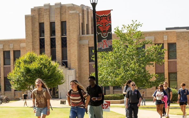 Sinh viên A-State đi bộ qua toà nhà Wilson Hall dưới lá cờ Red Wolves trong tuần đầu học kỳ mùa Thu