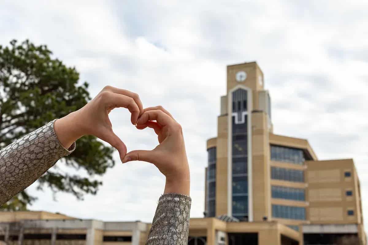 Student making a heart with hands in front of the A-State library clock tower