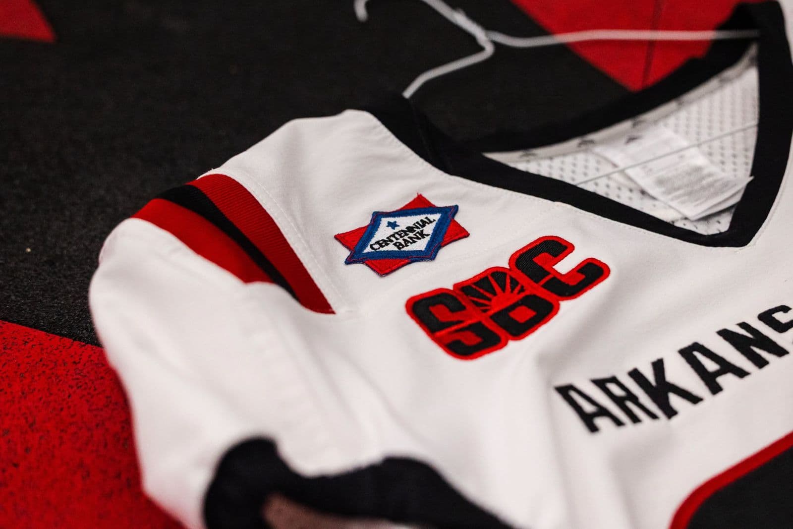 Cận cảnh logo Centennial Bank thêu trên vai áo đấu trắng của đội bóng bầu dục Arkansas State Red Wolves, bên cạnh logo Sun Belt Conference
