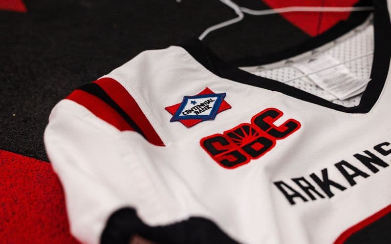 Cận cảnh logo Centennial Bank thêu trên vai áo đấu trắng của đội bóng bầu dục Arkansas State Red Wolves, bên cạnh logo Sun Belt Conference